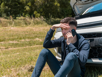 Junger Mann sitzt vor dem Auto und teilt seinen Motorschaden Ankauf mit. 